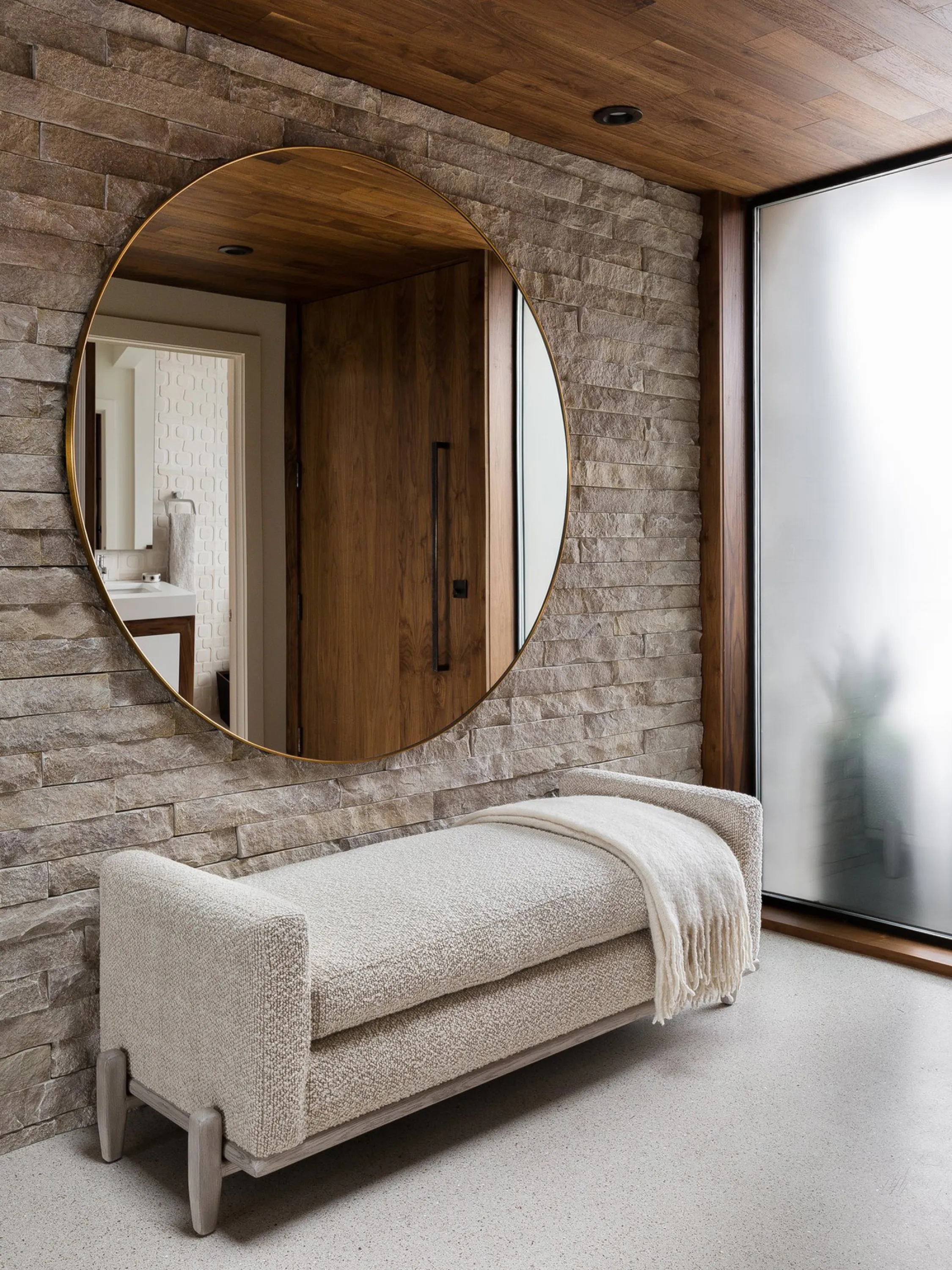 Entryway with a rough stone wall, wood ceiling and a soft welcoming bench.